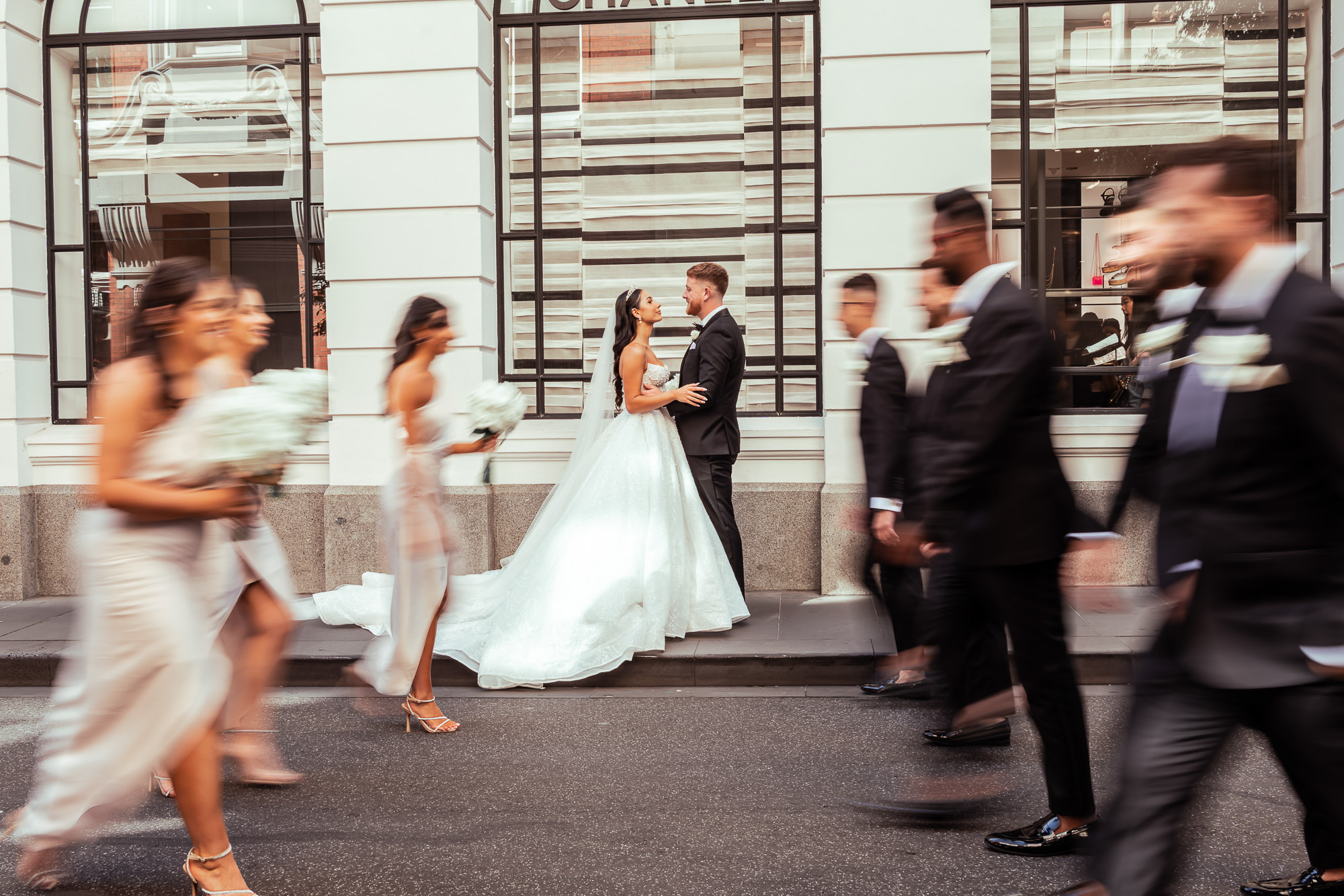 A Melbourne bridal party walks past a bride and groom outside Chanel, photographed by Royale Photography.